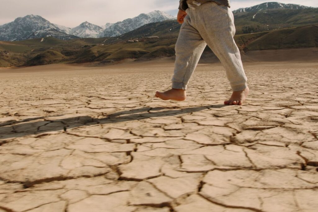 siccità, cambiamento climatico, bambino cammina a piedi nudi su terreno secco
