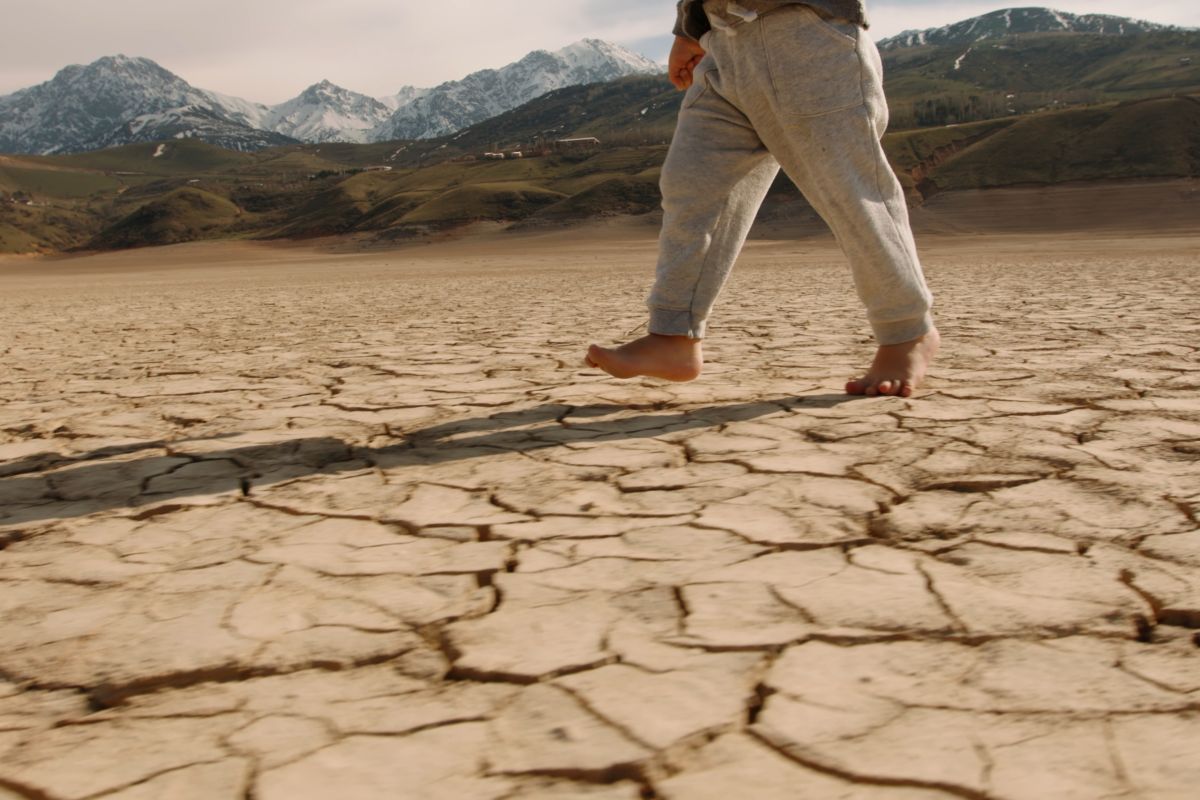 siccità, cambiamento climatico, bambino cammina a piedi nudi su terreno secco