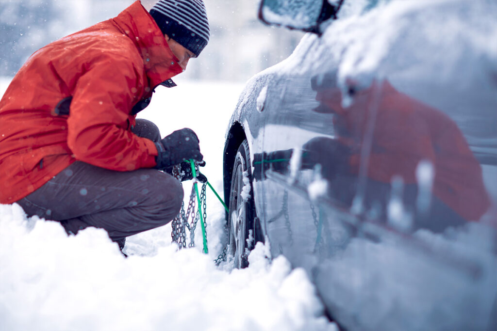 Uomo che tenta di montare le catene da neve alla sua auto