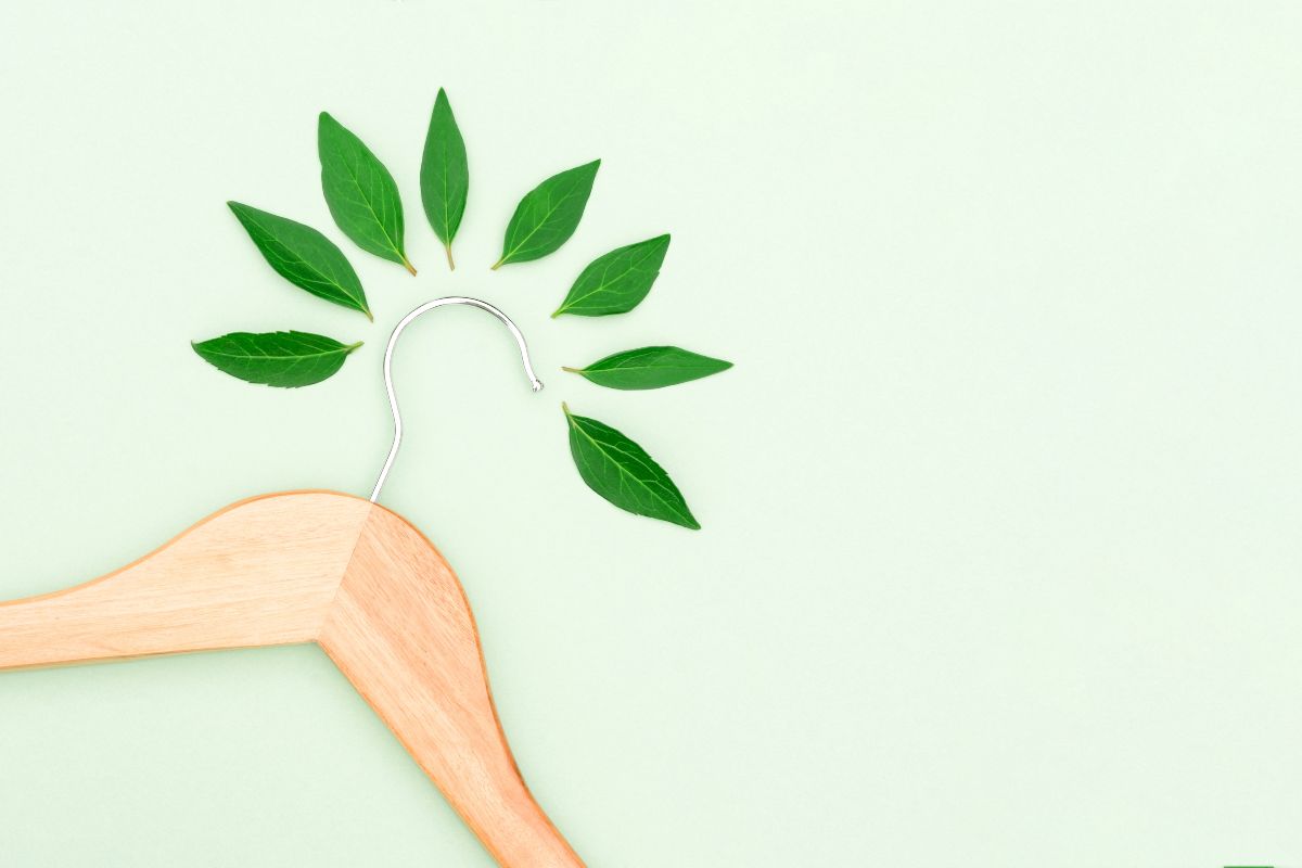 Concetto di moda sostenibile: appendiabiti su sfondo verde chiaro tra foglie naturali.