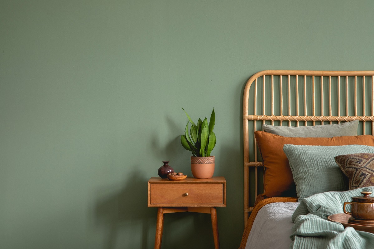 Dettaglio camera da letto: comodino e testiera in legno contro una parete verde scuro.