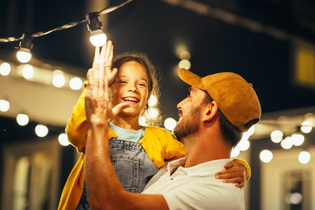 Tenerezza in famiglia: padre e figlia interagiscono con fili di luci luminose.