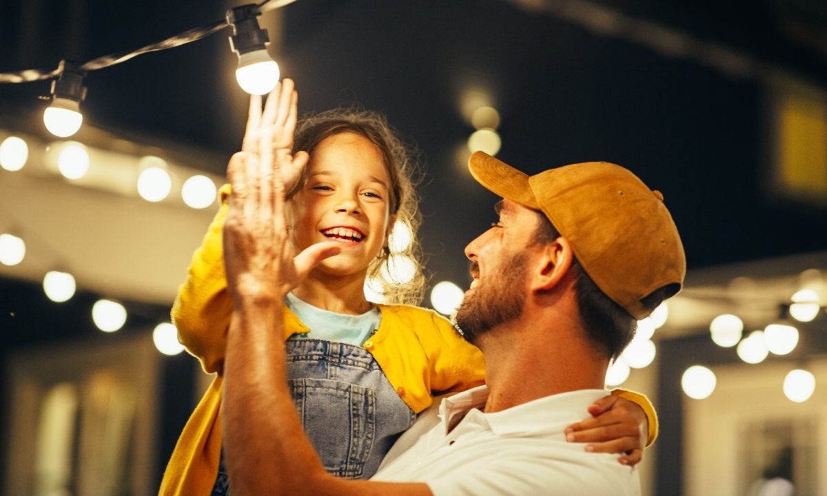 Tenerezza in famiglia: padre e figlia interagiscono con fili di luci luminose.