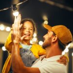 Tenerezza in famiglia: padre e figlia interagiscono con fili di luci luminose.