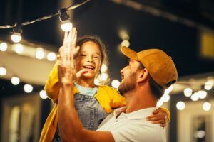 Tenerezza in famiglia: padre e figlia interagiscono con fili di luci luminose.