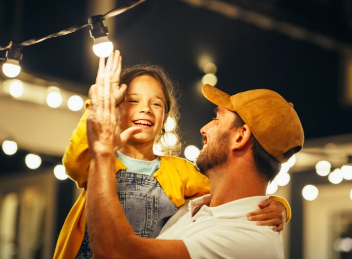 Tenerezza in famiglia: padre e figlia interagiscono con fili di luci luminose.