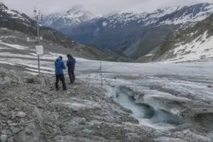 Due ricercatori vicino a una stazione meteo su un ghiacciaio in ritiro, con canale di acqua di fusione