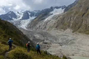 Tecnici in casco osservano un ghiacciaio in ritirata con detriti e pozze di fusione sotto le cime del Monte Bianco