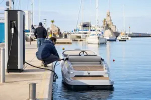Tecnico collega un cavo di ricarica a un piccolo runabout elettrico ormeggiato in un marina