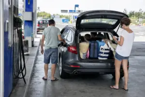 Famiglia fa rifornimento in un’area di servizio, auto con bagagliaio aperto pieno di valigie e borse da viaggio