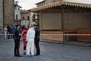 Carabinieri e soccorritore davanti a uno stand da festa transennato con nastro rosso e bianco in una piazza
