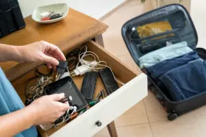 Mani che ordinano in un cassetto cavi, caricabatterie, pile esauste, telecomando e smartphone con schermo rotto, con