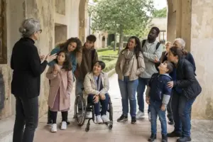 Gruppo di visitatori con bambini e una persona in sedia a rotelle ascolta una guida in un chiostro storico