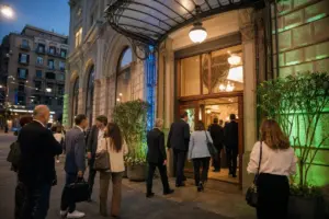 Partecipanti in abiti formali entrano in un teatro storico al tramonto, con piante in vaso e luci verdi e blu in facciata