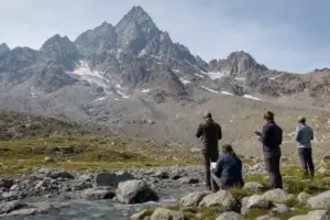 Ricercatori lungo un torrente alpino osservano il Monviso con chiazze di neve residue