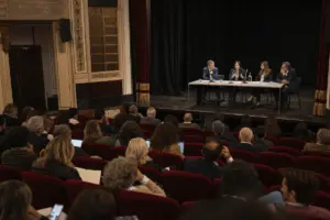 Panel di relatori su un palco teatrale davanti a un pubblico seduto su poltrone rosse